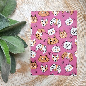 May include: Pink fabric with a repeating pattern of white and orange cats and dogs. The animals have simple, cartoon-like faces.