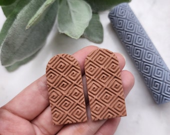 May include: A pair of terracotta-colored arch-shaped earrings with a geometric pattern. The earrings are made of polymer clay and have a textured surface.
