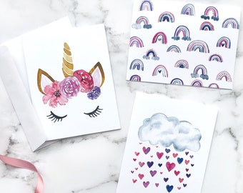 Set de tarjetas de felicitación de unicornio en acuarela: arcoíris y corazones, interior en blanco.