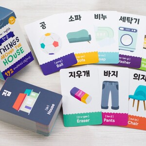 May include: A set of colorful flashcards with Korean and English words for household objects. The cards feature illustrations of a ball, sofa, soap, washing machine, bed, eraser, pants, and chair. The cards are part of a larger set of 192 cards.