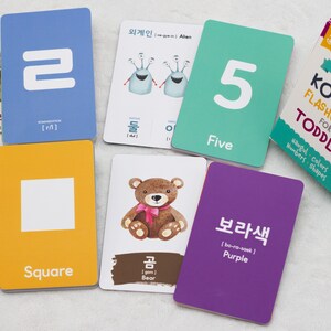 May include: A set of colorful flashcards for toddlers featuring Korean words, English translations, and illustrations. The cards include numbers, colors, shapes, and animals. The cards are part of a larger set titled "Korean Flashcards for Toddler".