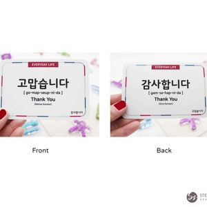 May include: Two white cards with red and blue borders. The front card says "고맙습니다" in Korean, which translates to "Thank You" in English. The back card says "감사합니다" in Korean, which also translates to "Thank You" in English. Both cards have the words "Everyday Life" printed on them.