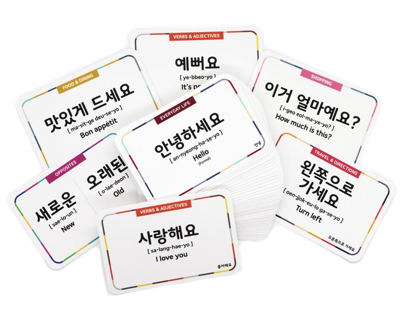 May include: A set of colorful flashcards with Korean words and their English translations. The cards feature various categories, including food and dining, everyday life, verbs and adjectives, shopping, and travel and directions. The cards are designed to help learners of the Korean language.