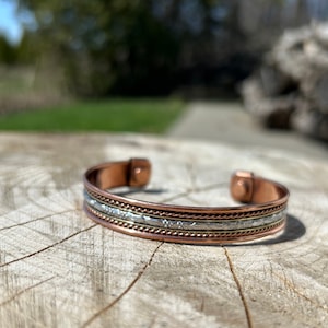 May include: A copper and silver bracelet with a textured design. The bracelet has a magnetic clasp.