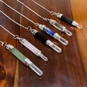 Puede incluir: Seis péndulos de cristal con cadenas plateadas y tapas decorativas. Los cristales son transparentes, verdes, rosas, negros, azules y transparentes con una punta negra.