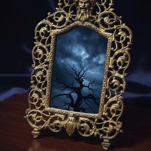 May include: An antique-style gold-coloured framed mirror. The frame has elaborate scrollwork and a sculpted face. The mirror reflects a dark, cloudy sky with a bare tree and a crescent moon, creating a gothic aesthetic.