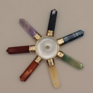 May include: A seven-pointed crystal chakra wheel with a white centre and gold accents. The points are made of different coloured crystals, including amethyst, lapis lazuli, green aventurine, citrine, red jasper, and black obsidian.