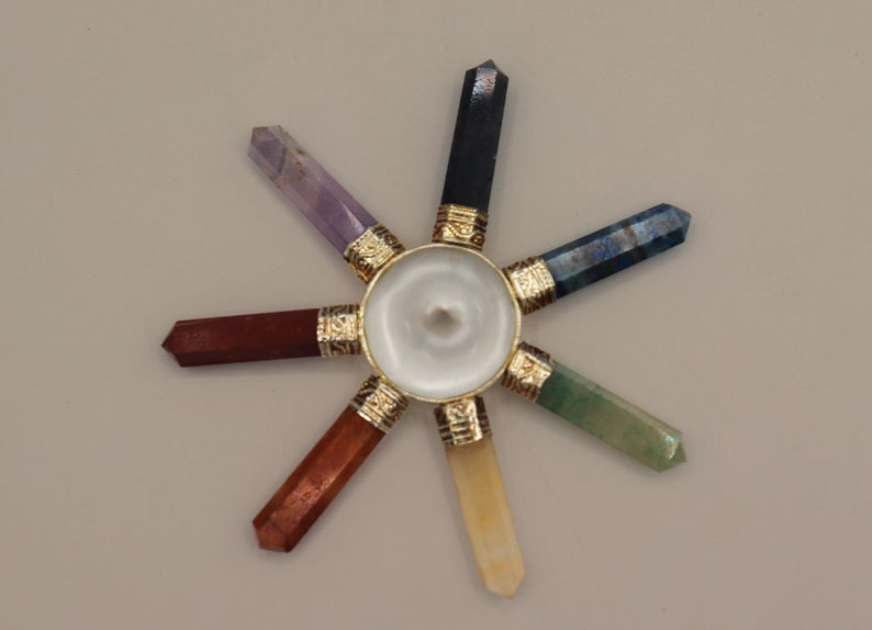 May include: A seven-pointed crystal chakra wheel with a white centre and gold accents. The points are made of different coloured crystals, including amethyst, lapis lazuli, green aventurine, citrine, red jasper, and black obsidian.
