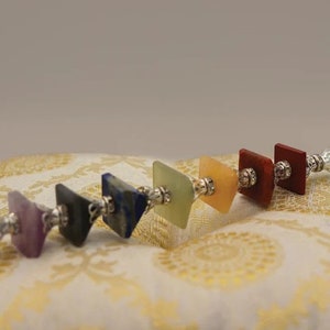 Puede incluir: Una varita de cristal con siete piedras de chakra en una secuencia de colores arcoíris. Las piedras están unidas a una varita de cristal transparente con detalles plateados.