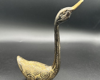 Può includere: Una statuetta decorativa a forma di cigno in ottone con intricati motivi incisi. Il corpo del cigno è adornato con disegni circolari, mentre il collo e il becco hanno una finitura a contrasto. Un oggetto di arredamento unico.