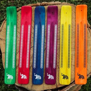 May include: Six wooden incense sticks with an elephant design at the bottom. The sticks are painted in different colours: green, red, blue, purple, yellow, and orange. Each stick has a white or black geometric pattern.