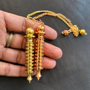 May include: Two metal pendulums with a gold and copper finish. The pendulums are attached to a chain with a small ball at the end.