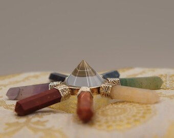 Può includere: Una piramide di cristallo trasparente con una base dorata si trova al centro di una stella a sette punte realizzata con pietre preziose lucidate. Le pietre preziose sono ametista, diaspro rosso, corniola, citrino, aventurina verde, sodalite blu e quarzo trasparente.