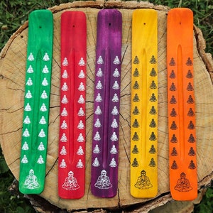 May include: Six wooden incense sticks with a Buddha design. The sticks are painted in different colours: green, red, purple, yellow, orange, and brown.
