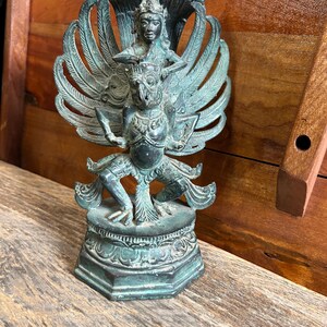 May include: A green bronze statue of a mythical creature with wings and a human figure riding on its back. The statue is on a wooden surface.