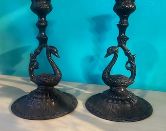 Puede incluir: Un par de candelabros de metal negro en forma de cisne. Los candelabros están detallados con diseños intrincados y tienen un aspecto clásico.