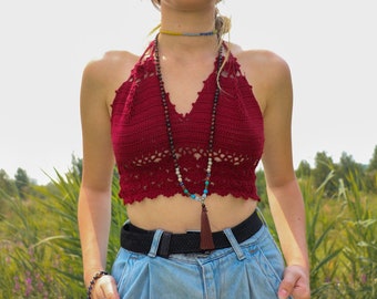 Puede incluir: Una mujer con un top rojo de ganchillo con un collar de cuentas y un cinturón negro sobre unos vaqueros azules.