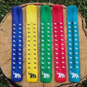 May include: Five wooden incense holders featuring elephant designs. The holders are painted in a variety of colours: blue, yellow, green, red, and turquoise.