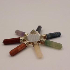 May include: A crystal chakra set with seven chakra stones arranged in a circle around a clear quartz pyramid. The stones are amethyst, red jasper, carnelian, yellow calcite, green aventurine, blue lapis lazuli, and clear quartz.