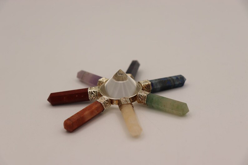 May include: A crystal chakra set with seven chakra stones arranged in a circle around a clear quartz pyramid. The stones are amethyst, red jasper, carnelian, yellow calcite, green aventurine, blue lapis lazuli, and clear quartz.