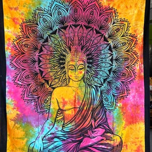 May include: A tie-dye tapestry featuring a black and white illustration of a meditating Buddha with a mandala behind him. The tapestry is a vibrant mix of pink, yellow, blue, and green.