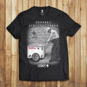 May include: Black t-shirt with a graphic of a street vendor pushing a cart with the text "Support Street Vendors" and "Paletero" on it. The graphic is in black and white with red accents.