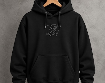 Peut inclure: Un sweat-shirt à capuche noir avec des manches longues, une poche kangourou sur le devant et des cordons de serrage noirs assortis. La poitrine présente le texte brodé Trust in God dans une police script ton sur ton. Le vêtement est sur un cintre.