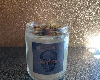 May include: A glass jar candle with a white wax base and a black and white label with a skull graphic and the text "Glitter Kids Craft Co. Samhain".
