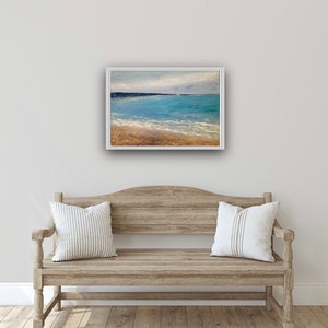 May include: A framed painting of a seascape with a blue ocean, white waves, and a sandy beach. The sky is a light blue with white clouds.