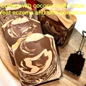May include: Close-up of several rectangular bars of soap with a marbled design in shades of brown and cream. The text on the image reads: "Coffee with coconut milk helps treat eczema and skin conditions."
