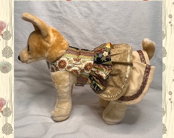 May include: A small dog wearing a brown and gold dog dress with a floral pattern. The dress has a ruffled skirt and gold trim.