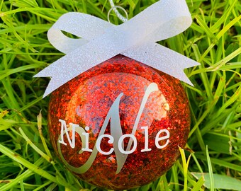 May include: Red glitter Christmas bauble with a white bow and the name "Nicole" written in silver lettering.