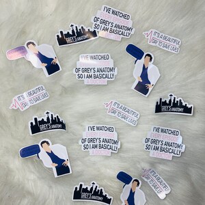 Może przedstawiać: Dziewięć naklejek z postacią z kresk&oacute;wki ubraną w niebieski fartuch chirurgiczny i biały płaszcz. Naklejki mają r&oacute;żne wzory, w tym panoramę miasta z tekstem "Grey's Anatomy", linię bicia serca z tekstem "To piękny dzień, aby ratować życie" oraz cytat, kt&oacute;ry brzmi: "Oglądałem każdy odcinek Grey's Anatomy, więc jestem zasadniczo lekarzem".