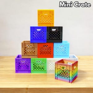 Könnte beinhalten: Eine Sammlung farbenfroher Mini-Kisten in verschiedenen Farbtönen, darunter Gelb, Blau, Schwarz, Braun, Rot, Hellblau, Lila, Grün, Weiß und ein Regenbogenverlauf. Der Text "Mini Crate" ist oben zu sehen. Diese Miniaturkisten sind pyramidenförmig angeordnet.