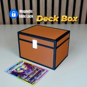 Può includere: Un portamazzo marrone con bordi neri e chiusura bianca, etichettato "Magnetic Slide Lock Deck Box". Una carta collezionabile colorata è davanti alla scatola. La scatola è progettata per conservare carte collezionabili.