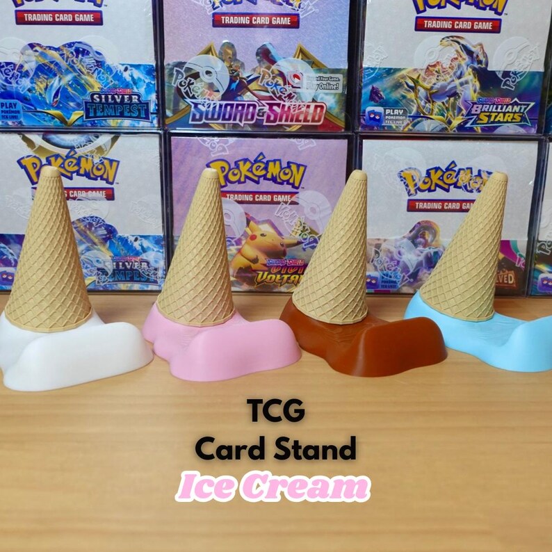 May include: Four colorful card stands shaped like ice cream cones. The stands are white, pink, brown, and blue, with a textured cone design. The text "TCG Card Stand Ice Cream" is displayed below the stands.