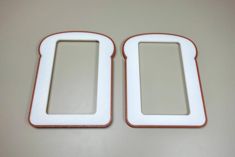 May include: Two flat, rectangular frames shaped like slices of bread. Each frame features a white center cutout surrounded by a brown border, mimicking the appearance of a crust. The objects are positioned side-by-side, displaying a consistent design.