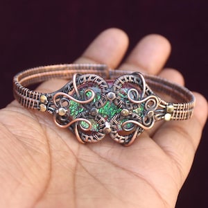 May include: A copper wire bracelet with a green and gold wire-wrapped stone in the center.