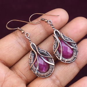 Pode incluir: Um par de brincos envoltos em fio de cobre com uma gema rosa em forma de lágrima no centro de cada brinco.