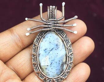 Peut inclure: Un pendentif en fil d'argent enroulé autour d'une pierre d'agate bleu clair et grise avec des inclusions noires. Le pendentif a la forme d'une araignée à huit pattes.
