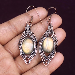May include: A pair of copper wire wrapped earrings with oval labradorite gemstones. The earrings have a delicate, intricate design.