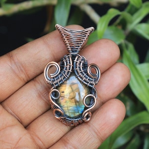 May include: A copper wire wrapped pendant featuring a labradorite gemstone. The pendant has a unique, intricate design with a copper and silver wire.
