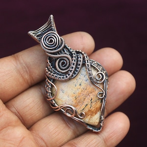 May include: A pendant featuring a brown and white agate stone wrapped in copper wire. The wire is twisted and formed into intricate designs, including spirals and loops.