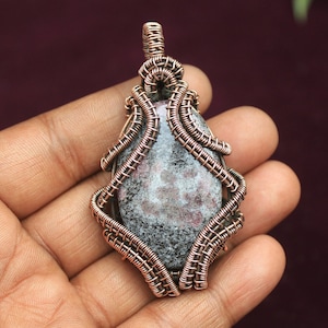 以下が含まれることがあります： グレーとピンクの斑点模様の石を、銅線で包んだペンダント