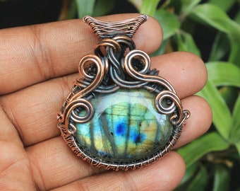 Puede incluir: Un colgante envuelto en alambre de cobre con una piedra preciosa de labradorita verde, azul y dorada.