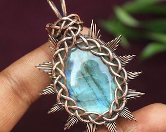 May include: A copper wire wrapped pendant featuring a blue-green labradorite gemstone. The pendant has a sunburst design with wire points radiating out from the center.