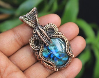 May include: A copper wire wrapped pendant featuring a blue-green labradorite gemstone. The pendant has a detailed, intricate design.