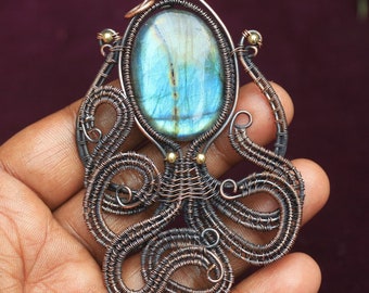 May include: A copper wire octopus pendant with a blue labradorite gemstone in the center. The octopus is made of wire wrapped around itself to create a three-dimensional design.