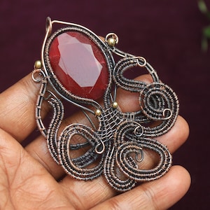 May include: A red gemstone pendant with a copper wire octopus design. The octopus is made of intricate wire coils and has a detailed design.