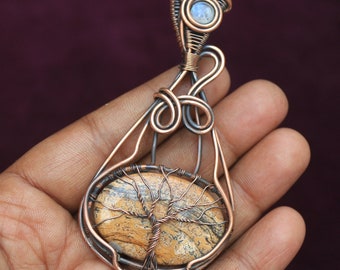 May include: A copper wire wrapped pendant featuring a brown and white tree agate stone with a tree design. The pendant has a copper wire loop at the top for hanging.
